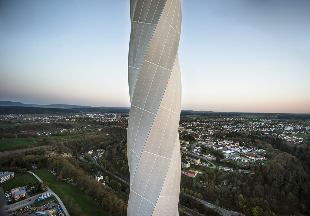 Über 200 Meter hoch, ist der Turm mit einer textilen Hülle umgeben, die den Betonschaft vor Sonneneinstrahlung schützt und den statisch unliebsamen Luftwirbeln auf Turm-Lee-Seite entgegen wirkt. (Bild: Rainer Viertlböck, Gauting)